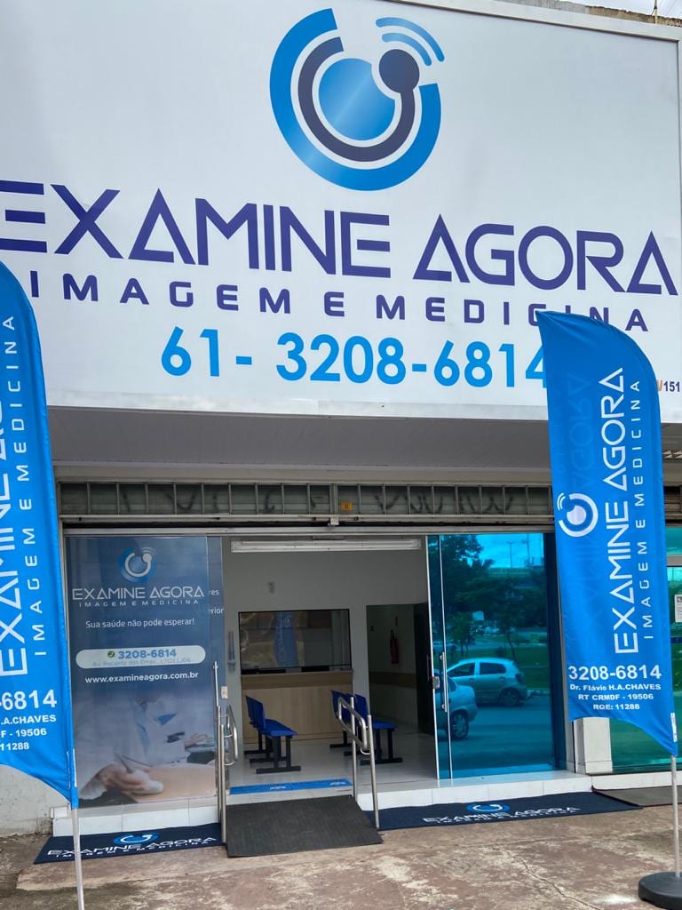 Entrada da Examine Agora em dia de atendimento, com as bandeiras da clínica na calçada